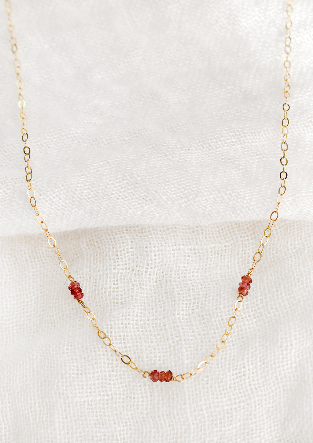Garnet: A delicate gold chain necklace with garnet beaded stations.