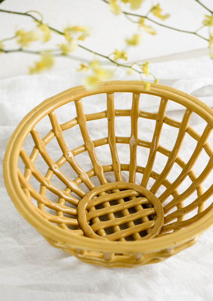 1: An open weave bowl made from mustard-colored ceramic.