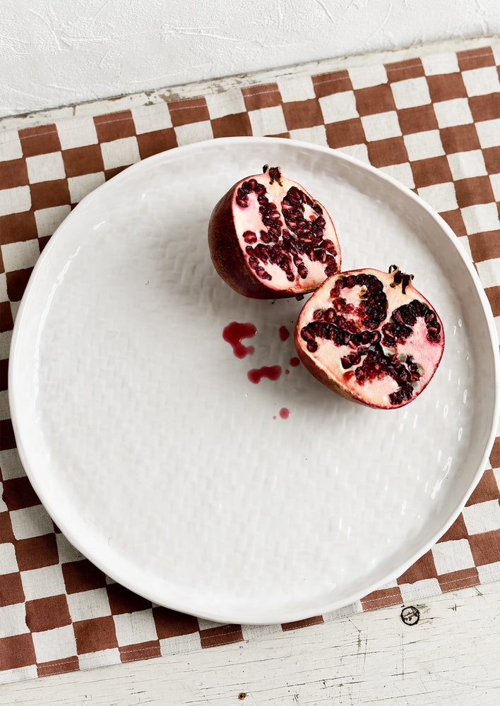 A round white ceramic tray with basketweave texture, styled with a pomegranate.