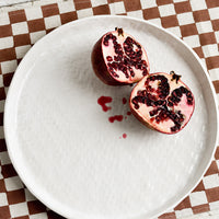 1: A round white ceramic tray with basketweave texture, styled with a pomegranate.