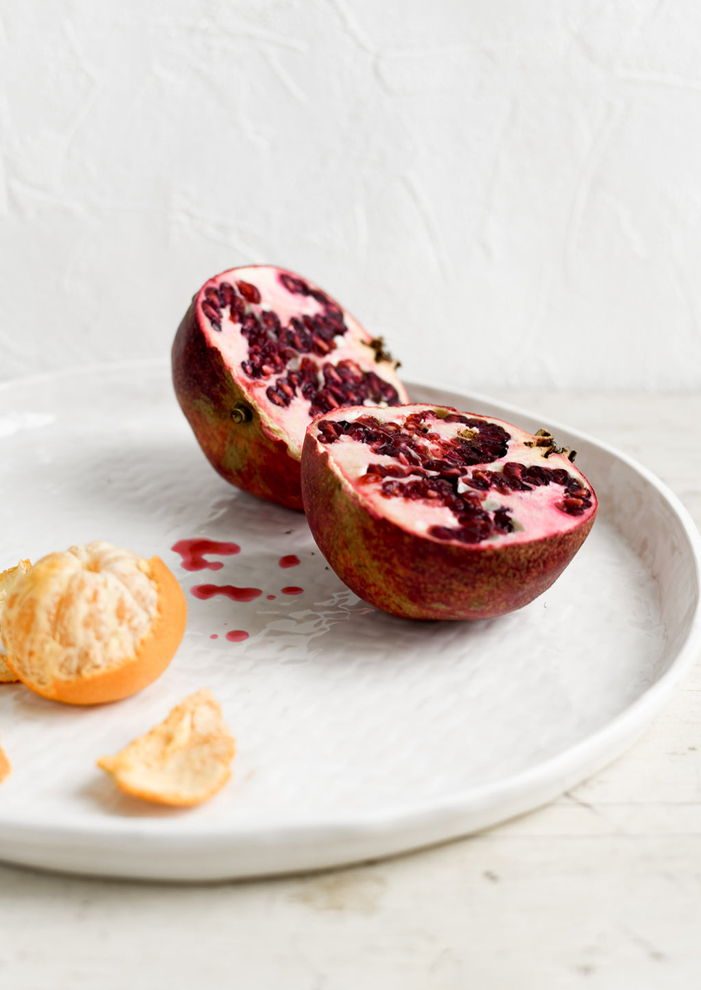 2: A round white ceramic tray with basketweave texture, styled with a pomegranate.