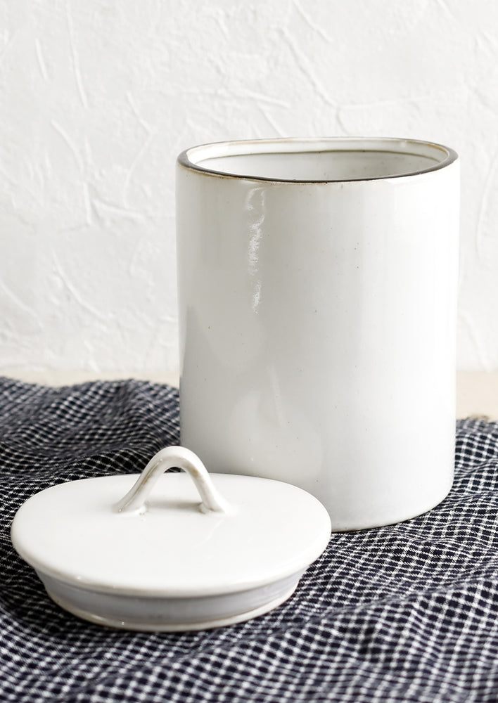A tall, cylindrical ceramic storage jar in glossy white glaze with removable lid.