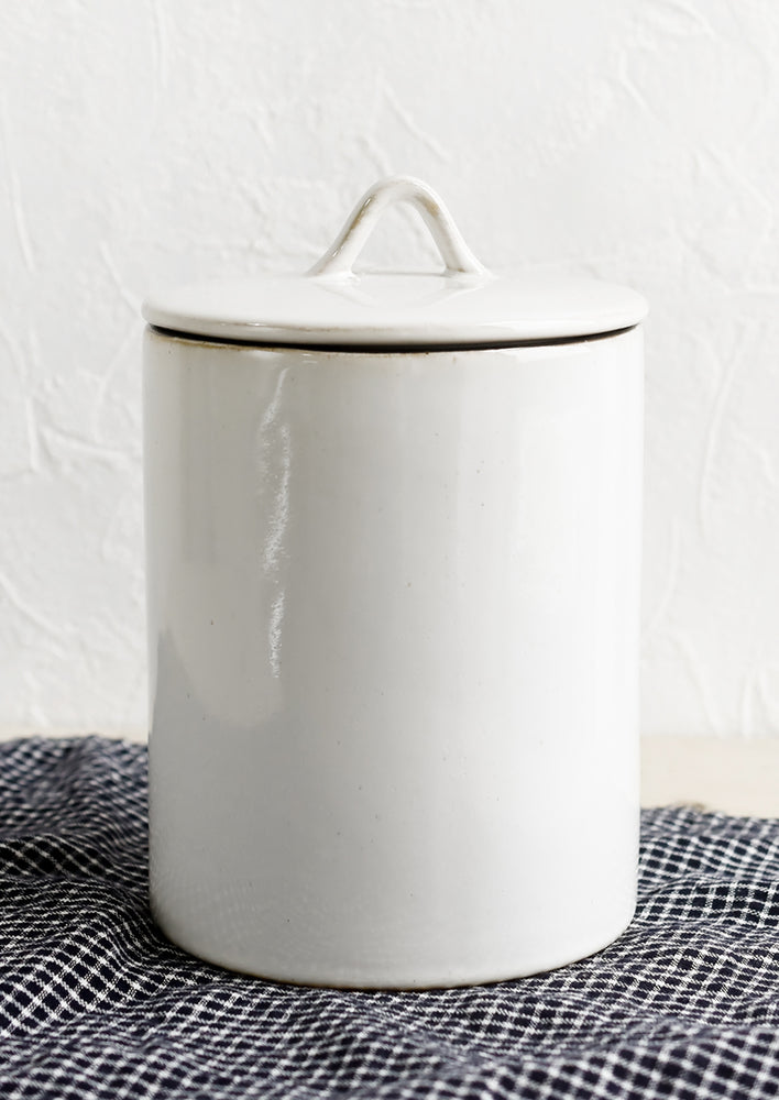 A tall, cylindrical ceramic storage jar in glossy white glaze with handled lid.