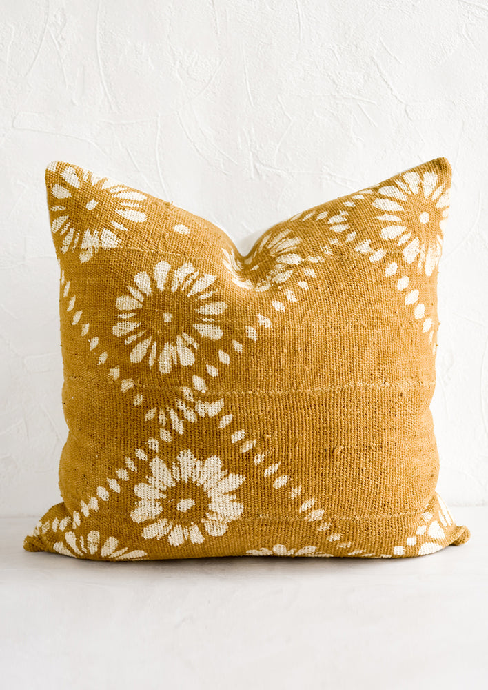 A mustard colored mudcloth throw pillow with white floral motif.