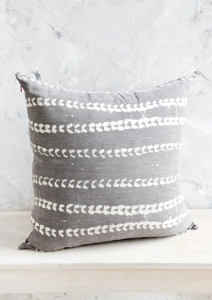 Square throw pillow in grey linen with horizontal batik print stripe pattern in white.