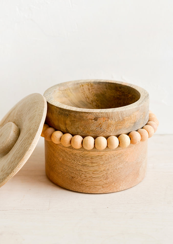 A round wooden storage box with lid and wooden beaded detailing.