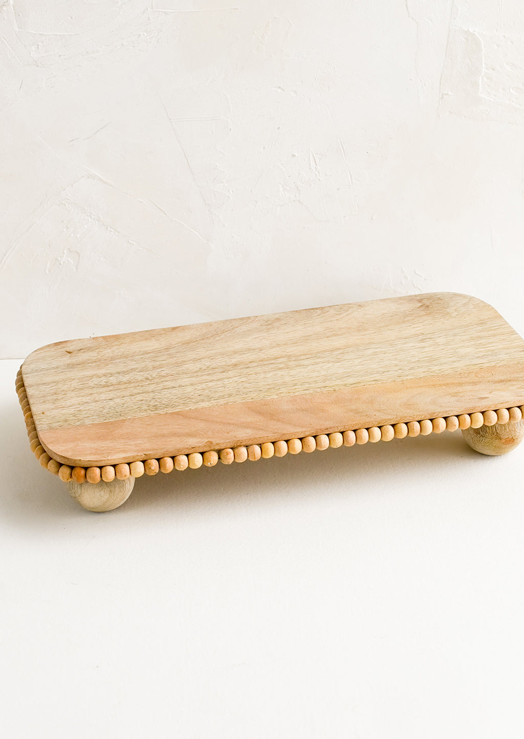 2: A rectangular wooden riser with round feet and beaded detail.