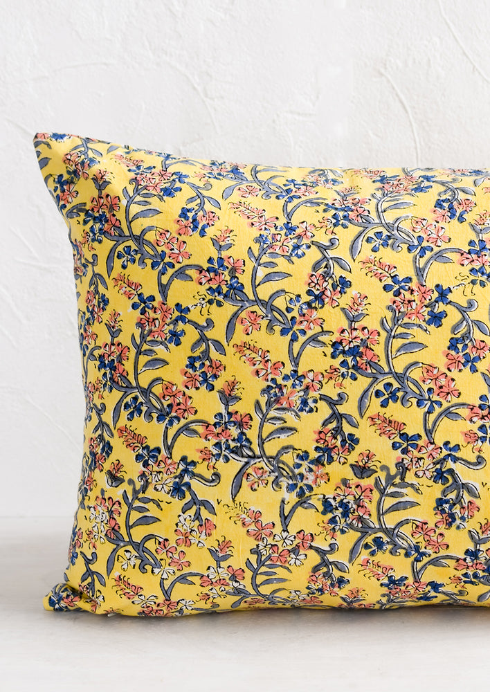 A block printed throw pillow in yellow with blue and pink floral print.