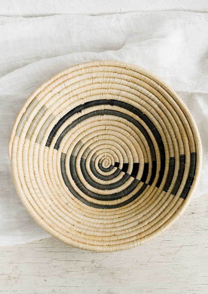 A round raffia bowl with grey spiral pattern.