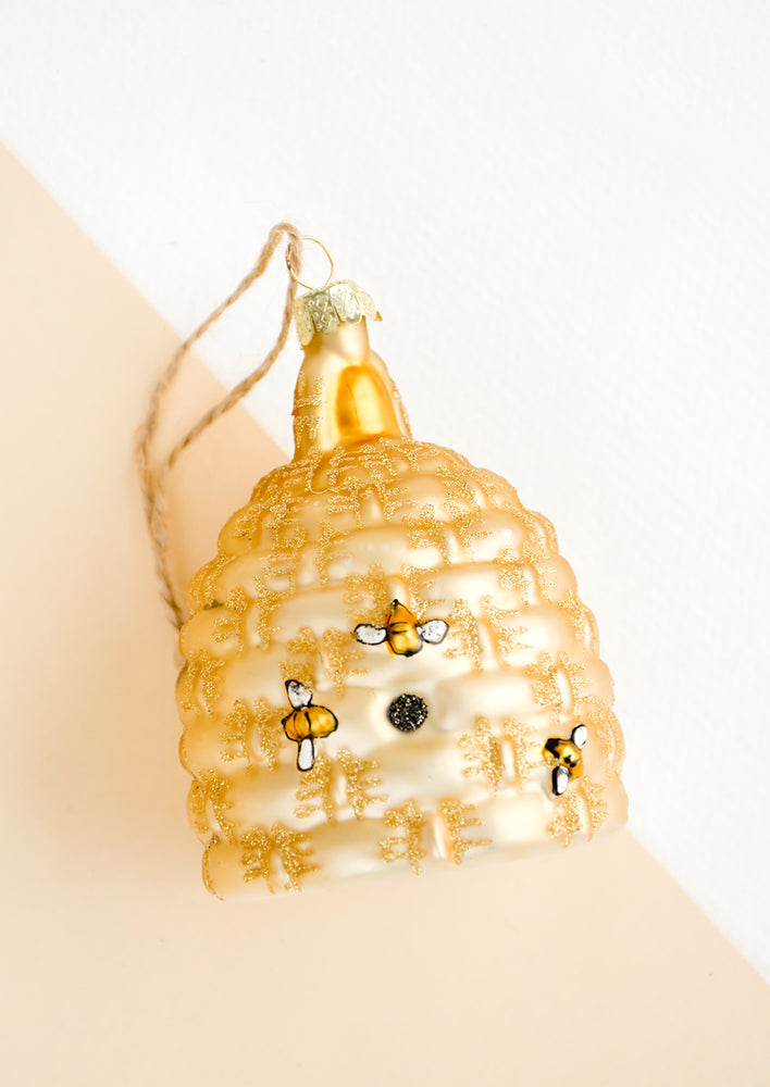 A glass ornament in the shape of a beehive with painted on bees.