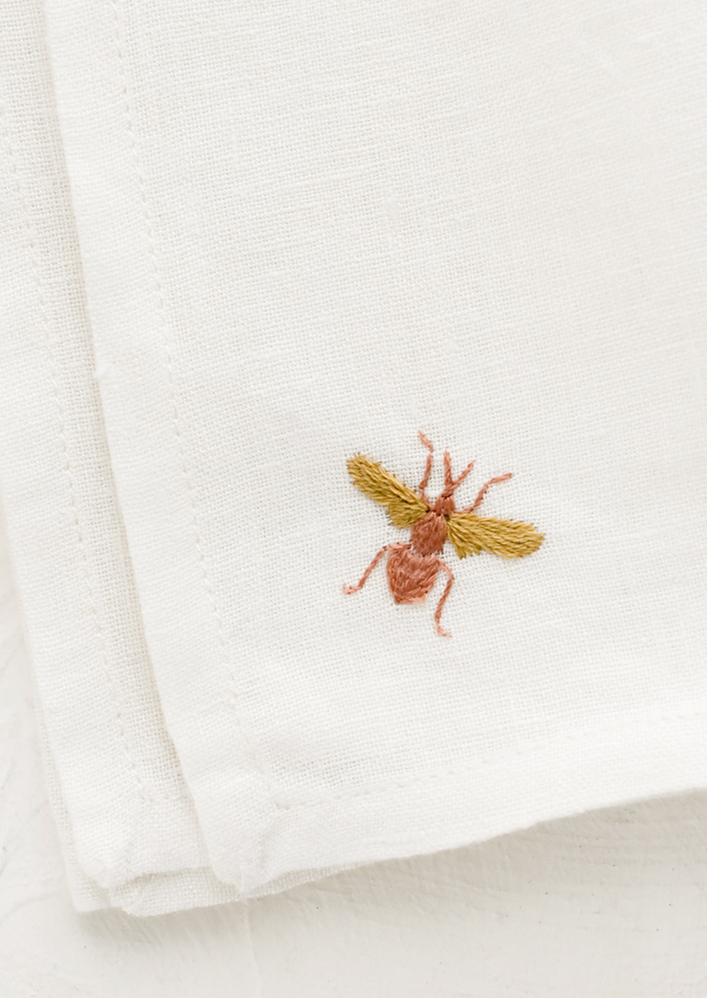 2: Embroidered bee on white linen.