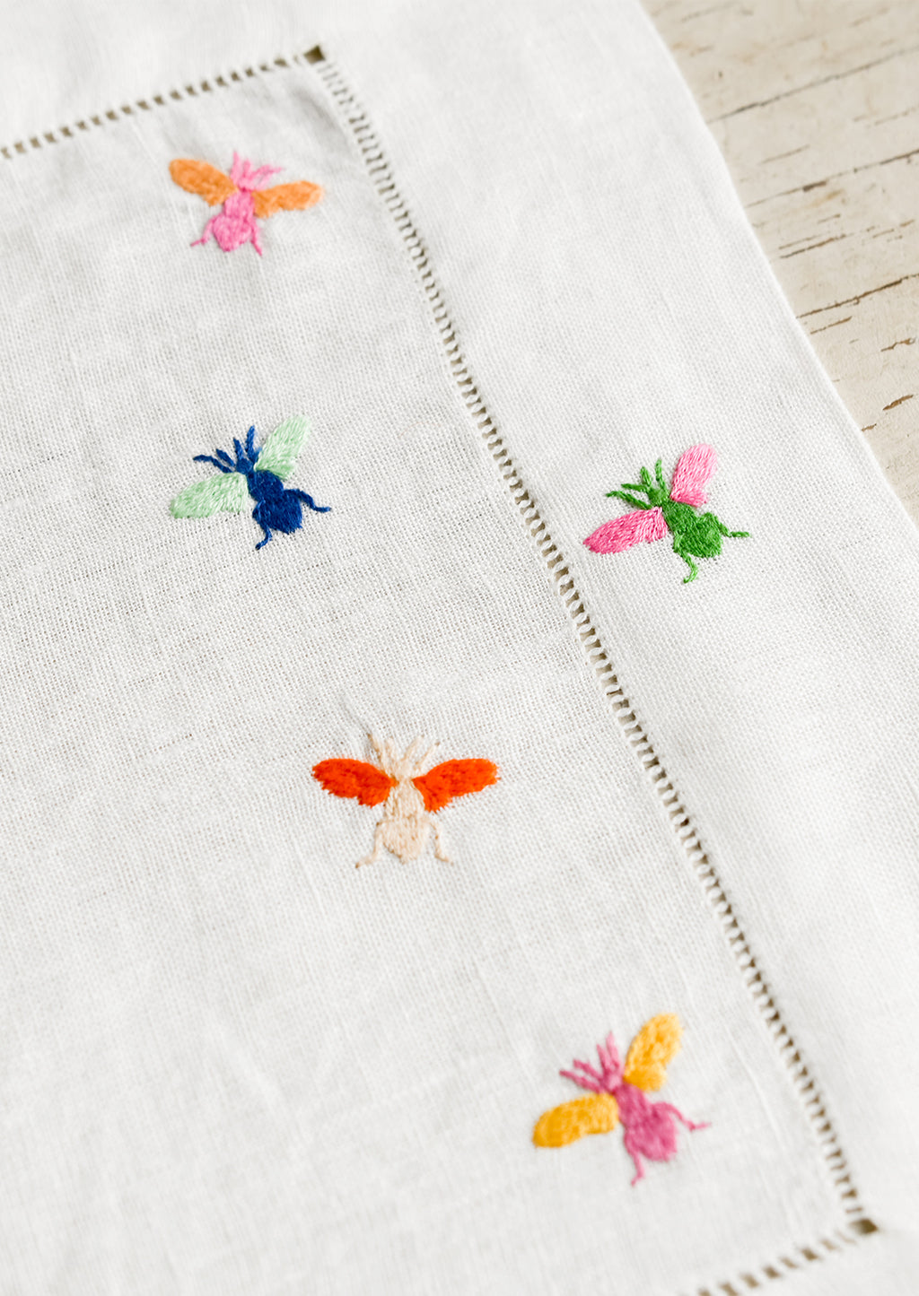 3: A white linen placemat with multicolor bee embroidery.