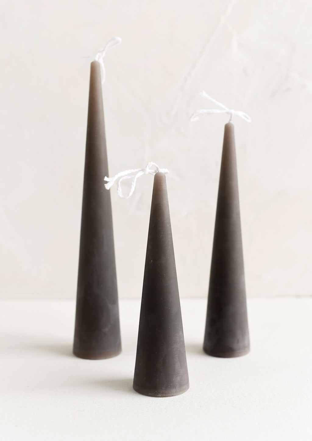 Small / Stone: Three lit cone-shaped taper candles in dark grey.