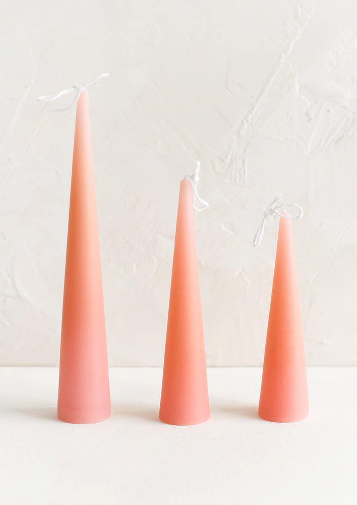 Small / Pink Peach: Three lit cone-shaped taper candles in pink peach.