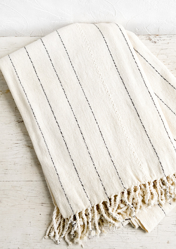 A natural cotton blanket with thin back stripes and braided trim.