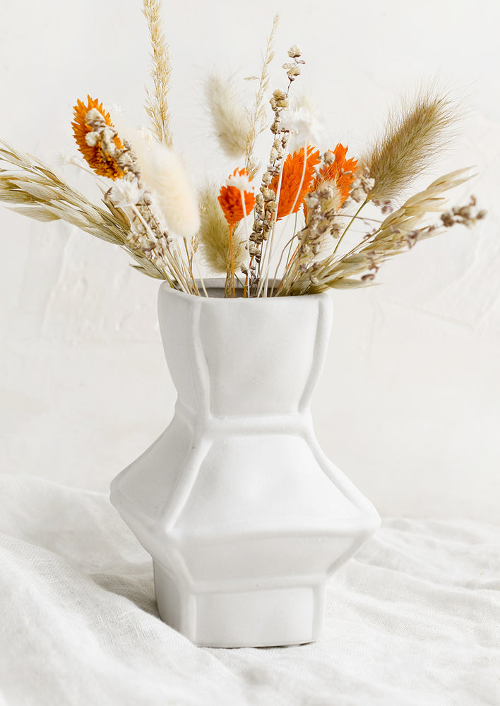 Short: A short geometric vase in white ceramic, shown with dried flowers.