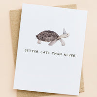 1: A greeting card with illustration of a tortoise in a party hat, text underneath reads "Better late than never".