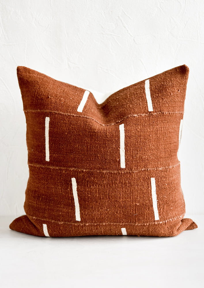 A mudcloth throw pillow in rust with white vertical line motif.