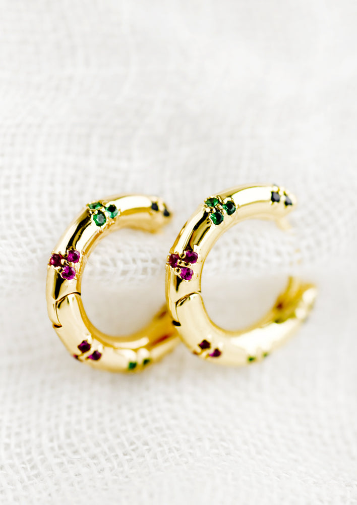 1: A pair of gold huggie hoops with colored crystal detailing.