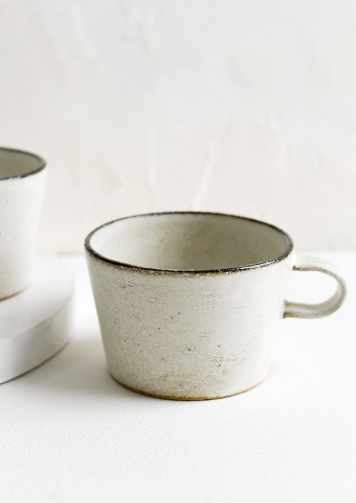 1: A small ceramic mug in tan glaze with dark rim.