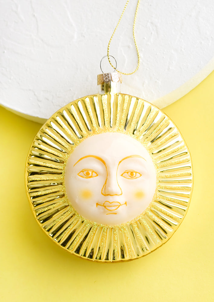 A decorative holiday ornament in shape of sun with smiling face.