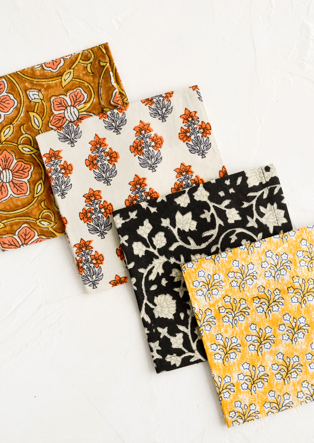 1: Four square fabric cocktail napkins in assorted colors and patterns.
