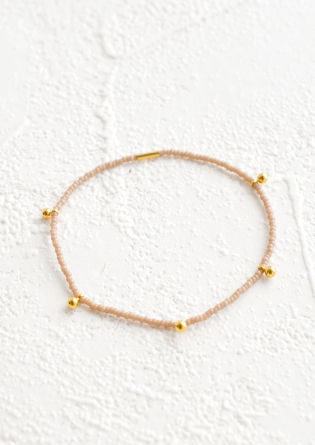 Chai: Bracelet made from tan colored glass seed beads with brass ball accent charms and logo tag