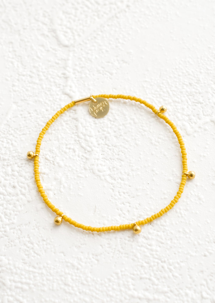 Bracelet made from mustard colored glass seed beads with brass ball accent charms and logo tag