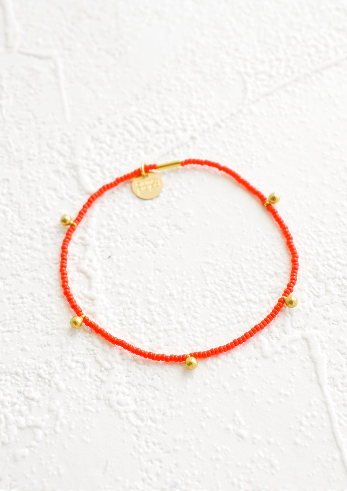 Poppy: Bracelet made from red colored glass seed beads with brass ball accent charms and logo tag