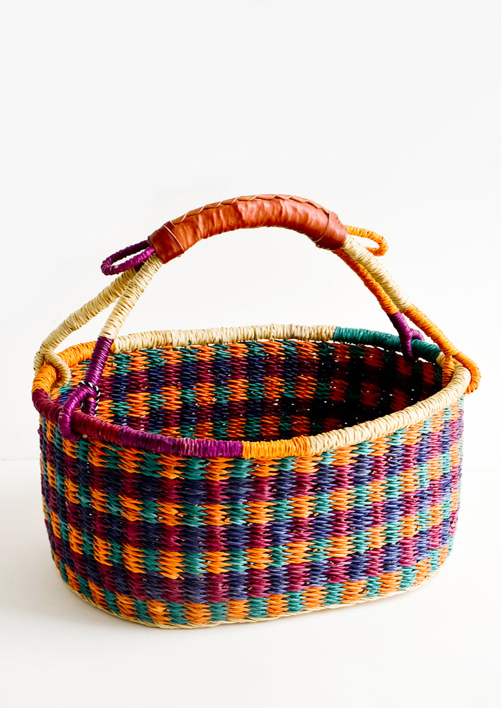 Woven basket made from multicolor dyed elephant grass with leather wrapped carrying handle