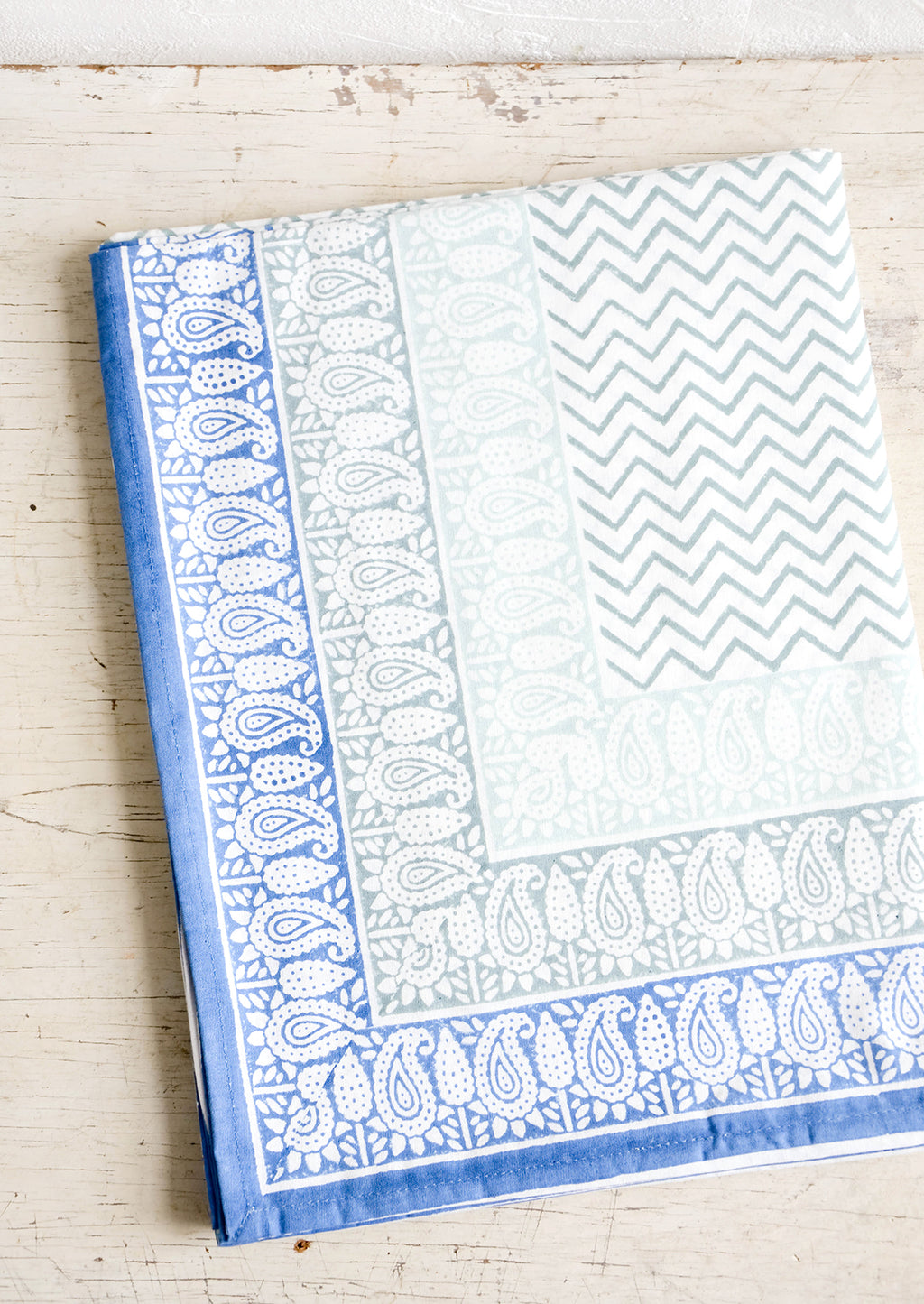 1: Chevron patterned tablecloth with paisley border in shades of blue, folded on a table