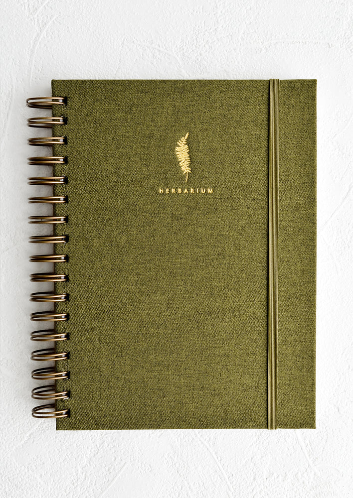 A cloth covered spiral bound journal with gold foil fern and "Herbarium" in small text.