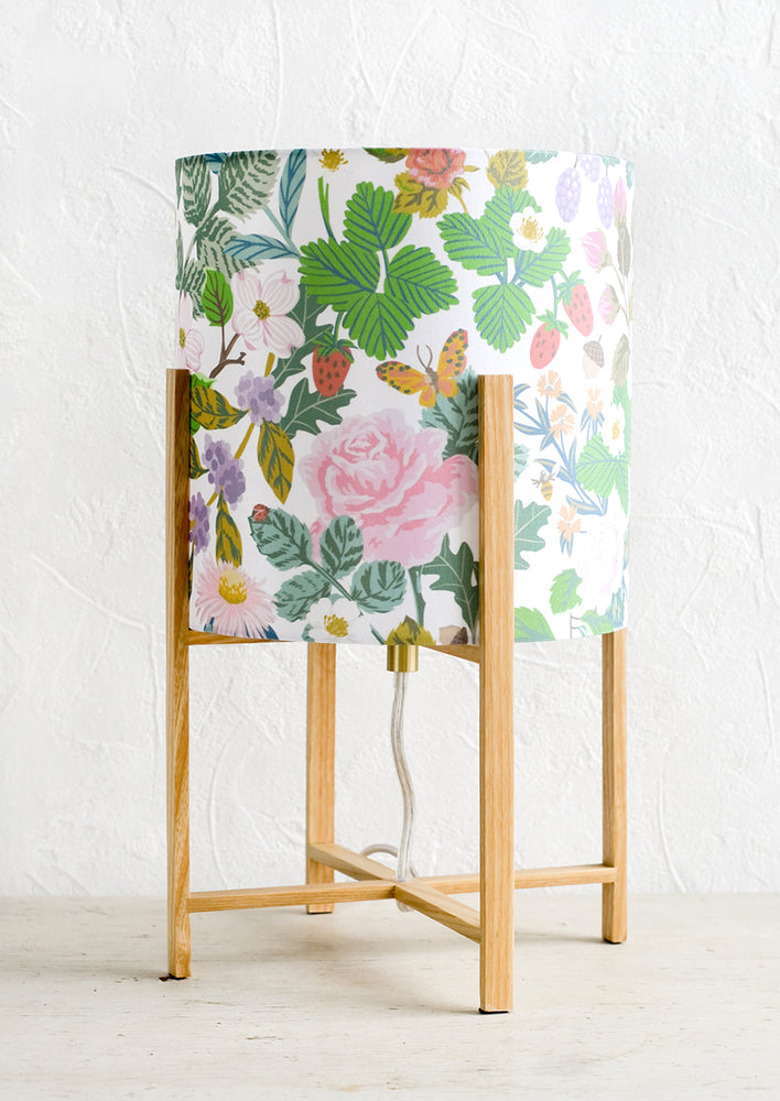 A table lamp with minimal oak base and botanical print shade.