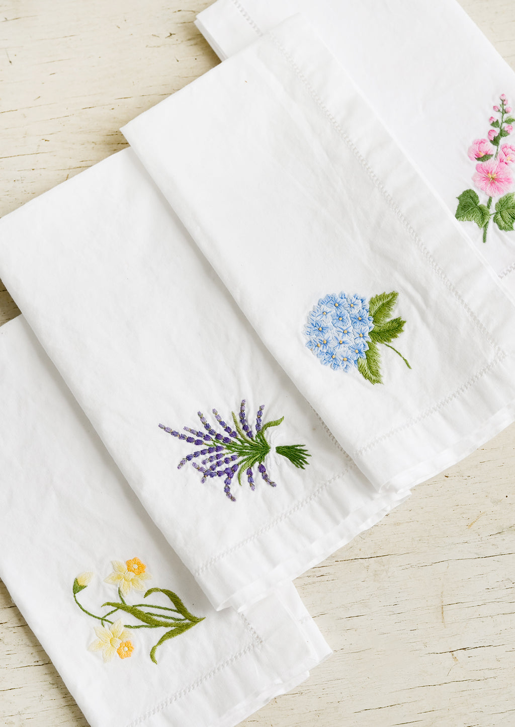 2: Four white cotton napkins with colorful botanical embroidery.