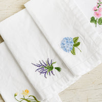 2: Four white cotton napkins with colorful botanical embroidery.