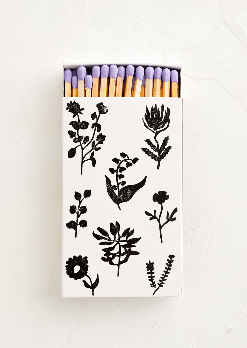 2: A matchbox in white with black botanical print, housing purple tipped matches.