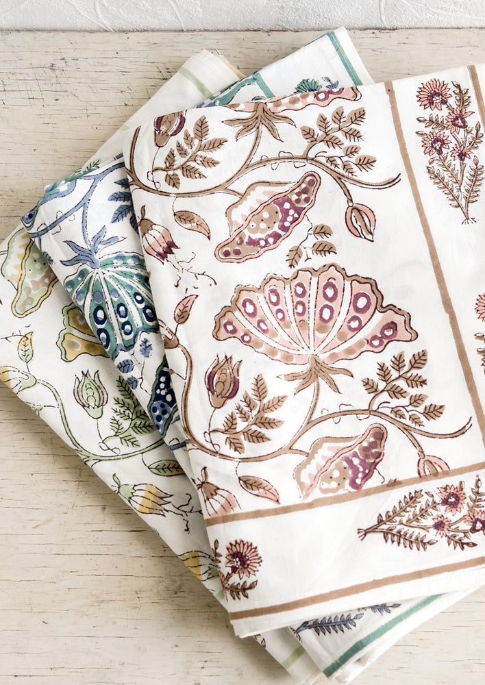 A stack of botanical block printed tablecloths in three colors.