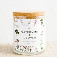 Watermint & Clover: A glass candle with a cork lid and white botanical printed label reading "watermint and clover".