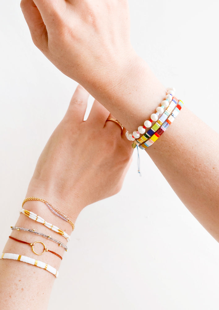A woman's hands crossed with her wrists featuring many different bracelets.