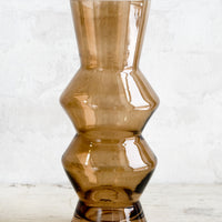 1: A tall glass vase in brown glass with zig zag silhouette.