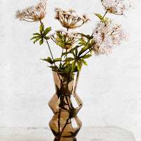 2: A brown glass vase holding tall flowers resembling Queen Anne's Lace.