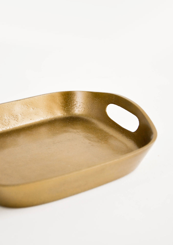 Square catchall tray in unpolished brass with raised sides, cutout handles at two sides