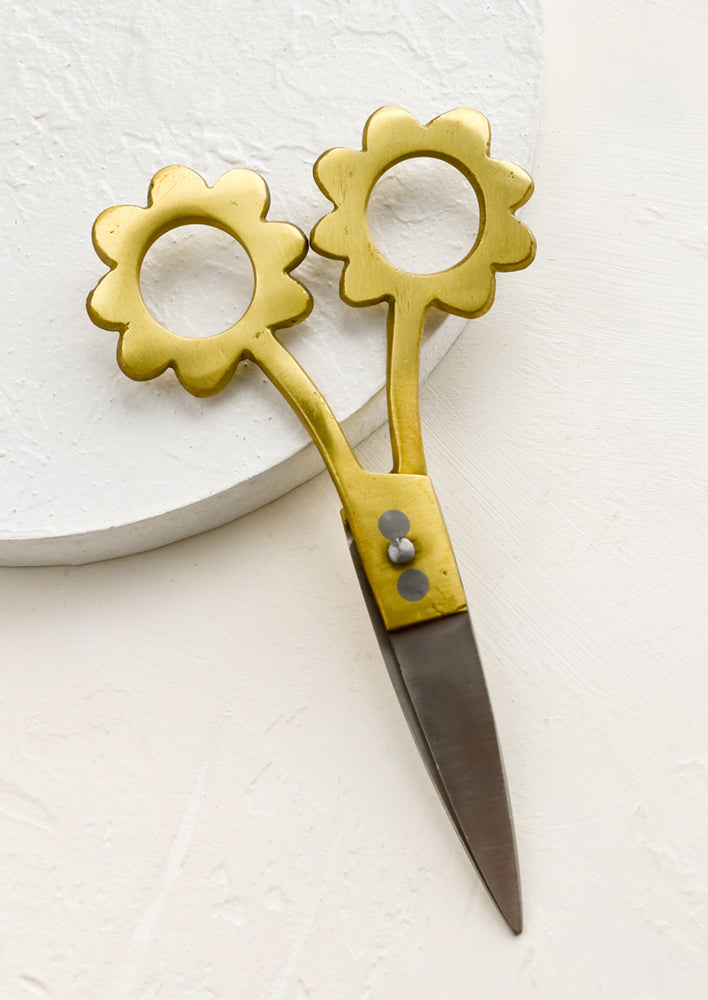 A pair of stainless steel scissors with brass flower shaped handles.