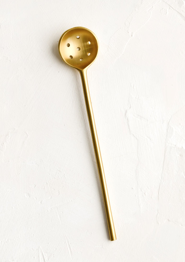 A slender slotted spoon in brushed brass.