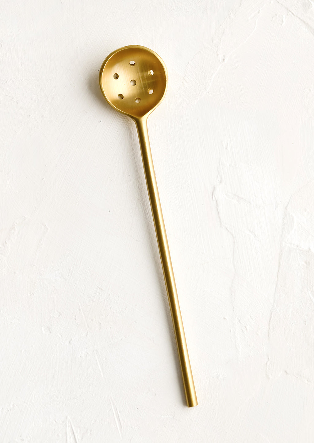 1: A slender slotted spoon in brushed brass.