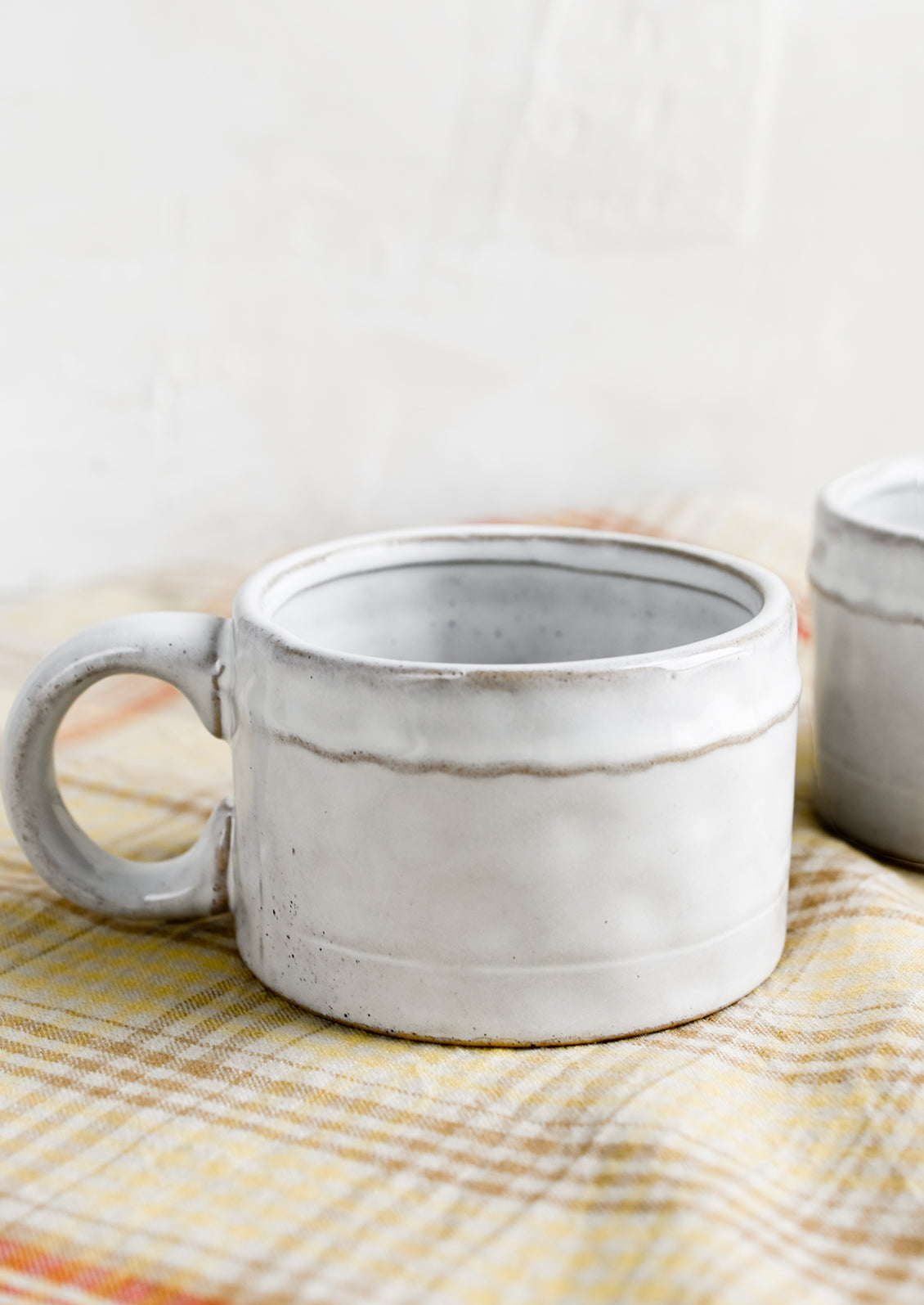 A ceramic mug in glossy white glaze with single wavy line detail.
