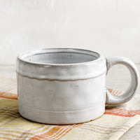 2: A ceramic mug in glossy white glaze with single wavy line detail.