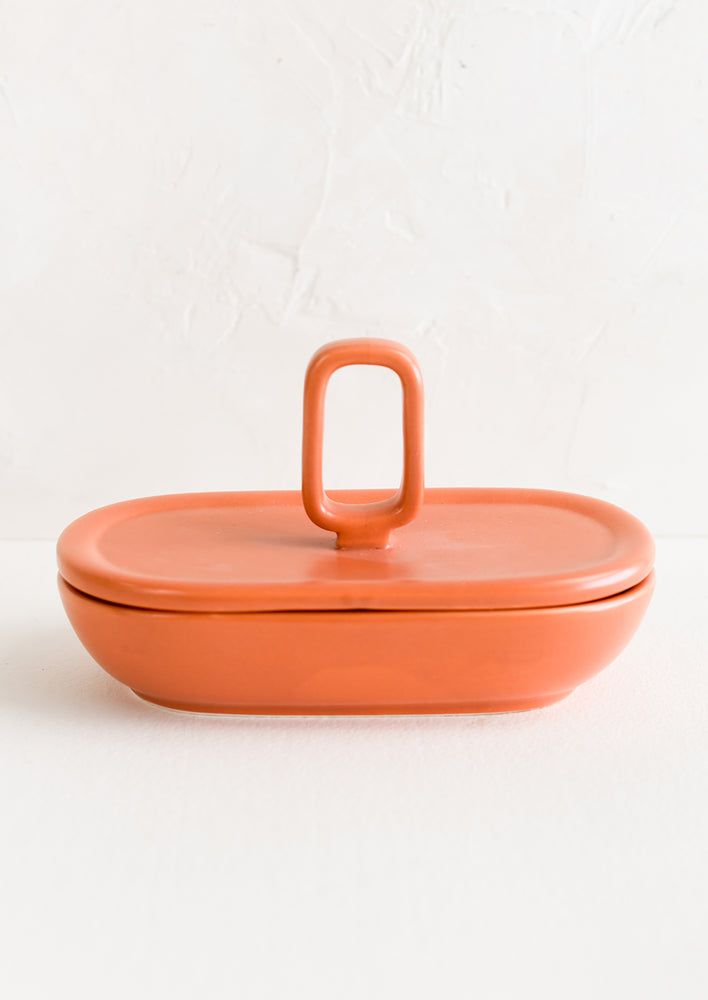 An oval shaped lidded ceramic container in papaya orange.