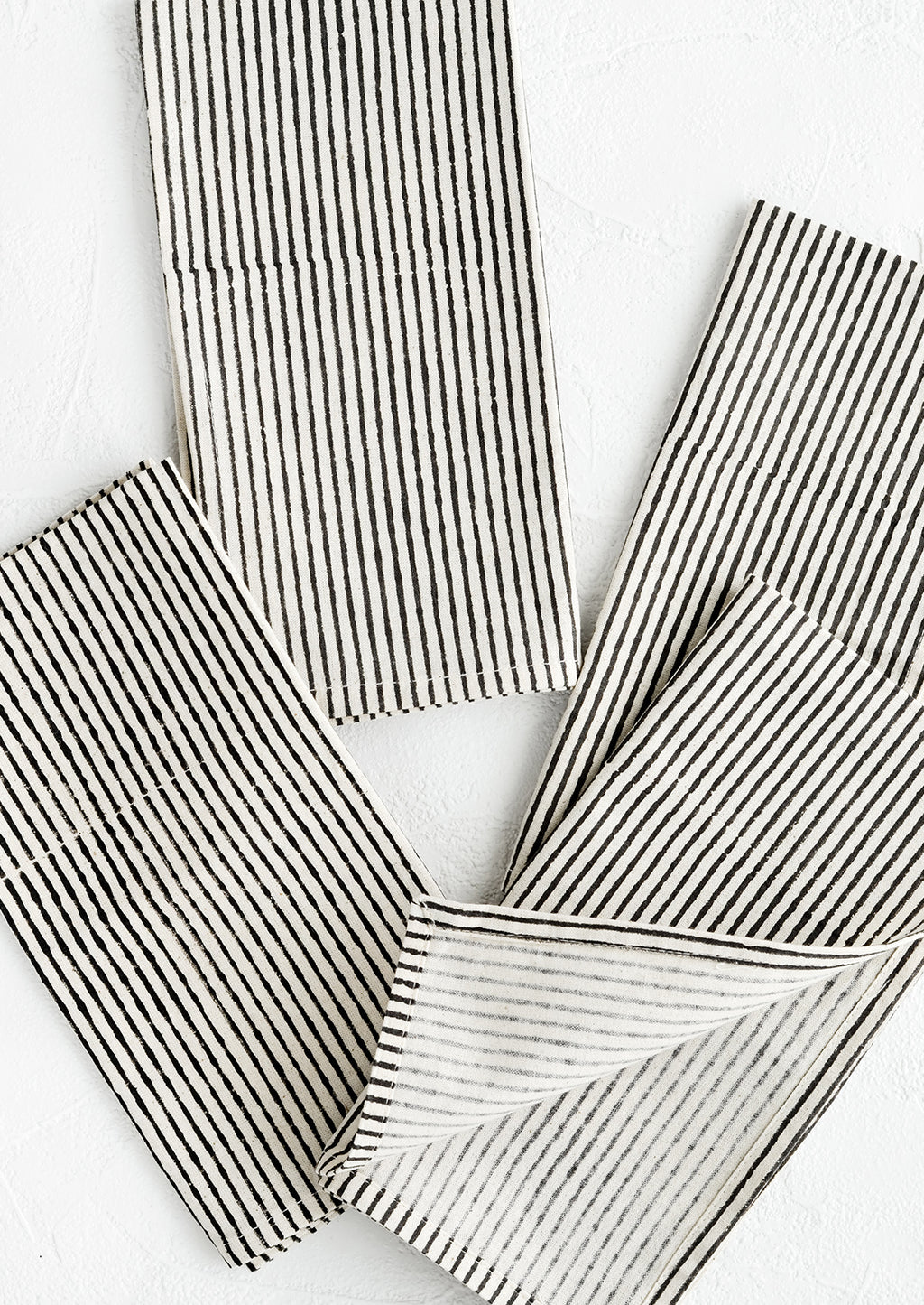 1: Scattered folded fabric napkins in natural cotton with hand-drawn line pattern in black.