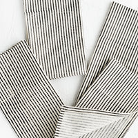 1: Scattered folded fabric napkins in natural cotton with hand-drawn line pattern in black.